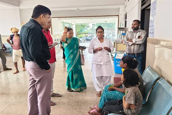 छात्रावास के बरामदे में अधिकारी और कर्मचारी बैठी हुई छात्राओं से बातचीत करते हुए